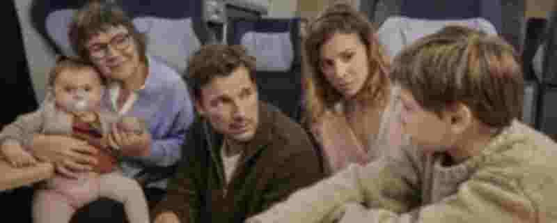 Ein Baby auf dem Arm einer älteren Frau, ein Mann, eine weitere Frau und ein Kind sitzen in einem Zug